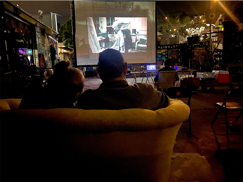 folks on couches and chairs watching an outdoor film on a screen